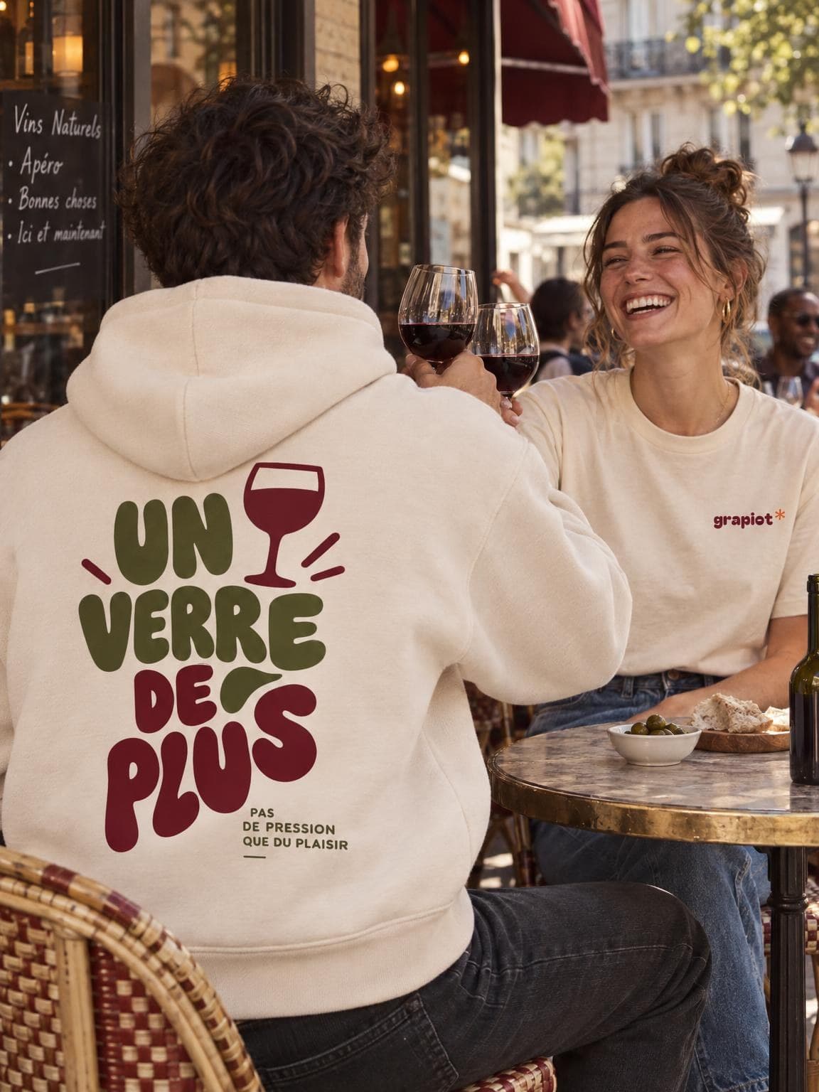 Deux amis trinquent en terrasse, dos imprimé Un Verre de Plus sur un hoodie crème